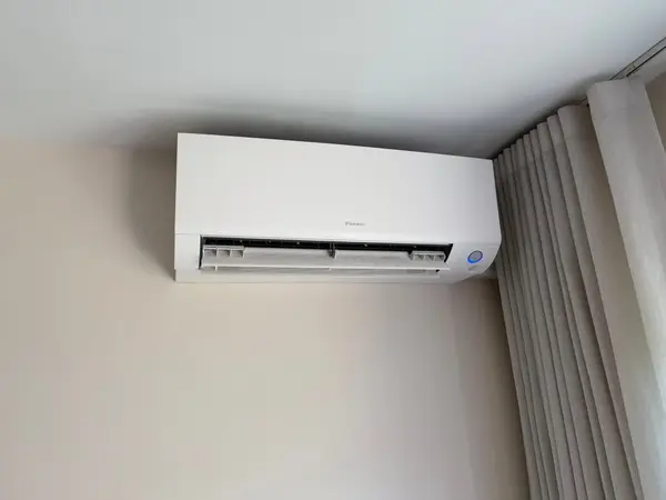 Wit Daikin airco-binnendeel hoog tegen de wand gemonteerd, naast de gordijnrail