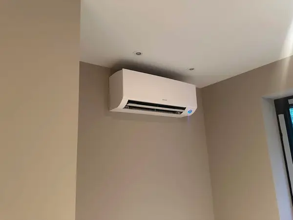 Wit Daikin airco-binnendeel hoog in de hoek van een woonkamer, naast inbouwspots