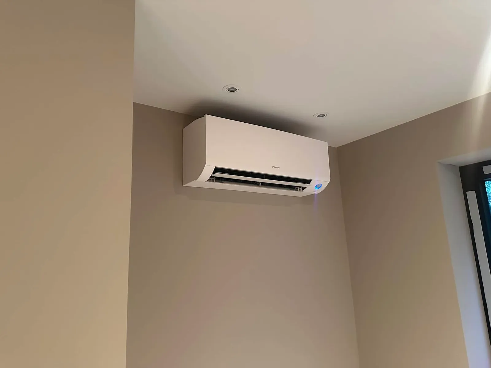 Wit Daikin airco-binnendeel hoog in de hoek van een woonkamer, naast inbouwspots