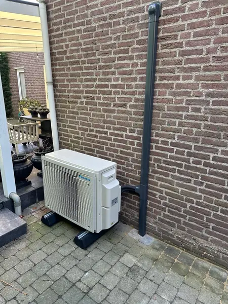 Airco-buitenunit met nette leidinggoot langs de gevel bij een patio