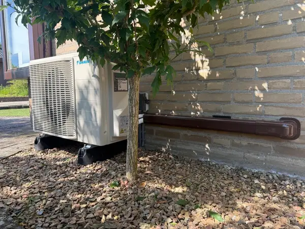 Daikin-buitenunit discreet geplaatst in een tuin onder een boom