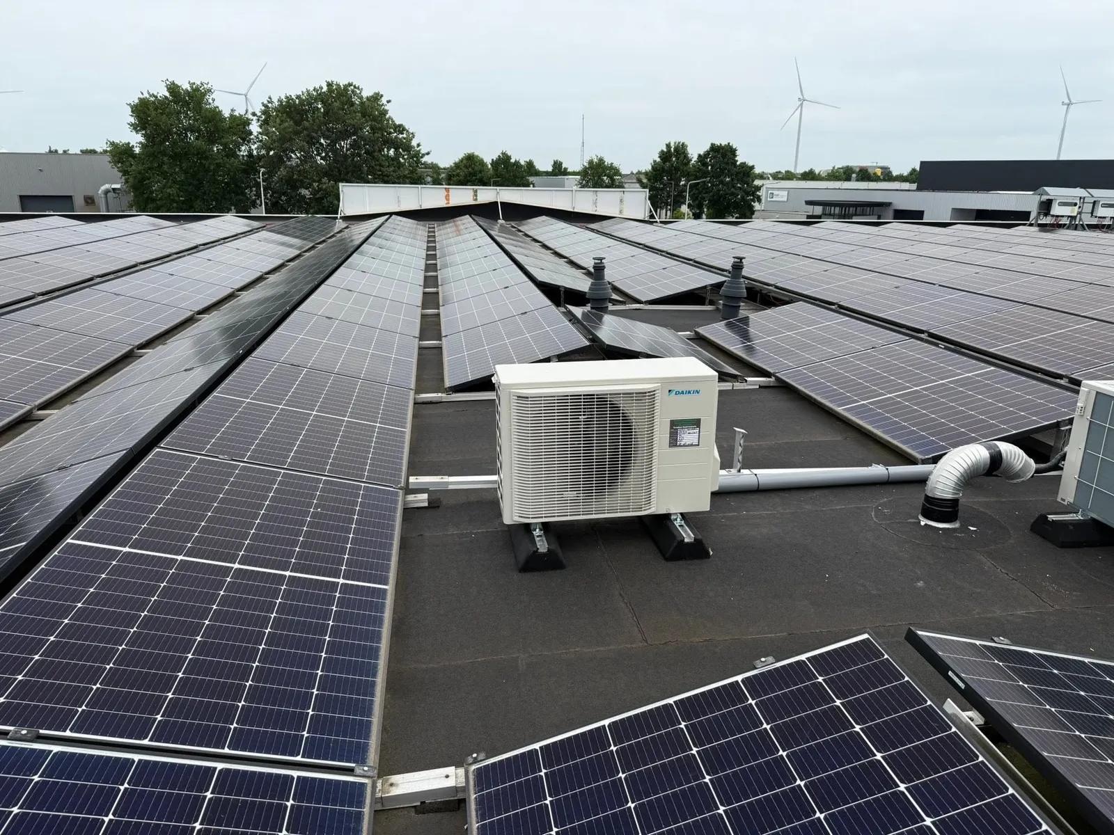 Daikin-buitenunit op het platte dak van een bedrijfspand, tussen de zonnepanelen