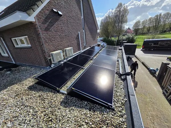 Zwarte zonnepanelen op een plat grinddak, met twee Daikin airco-buitenunits tegen de gevel