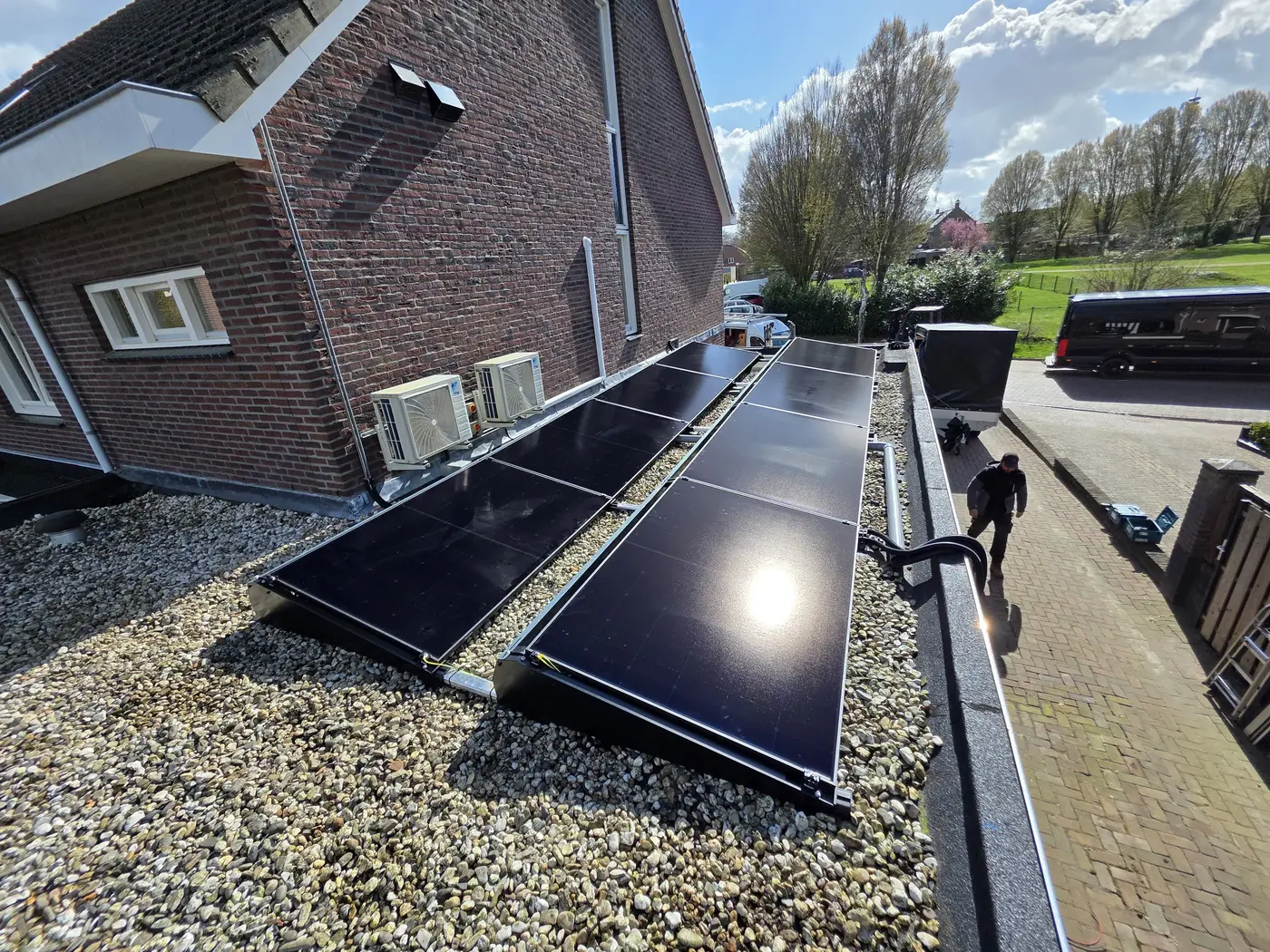 Zwarte zonnepanelen op een plat grinddak, met twee Daikin airco-buitenunits tegen de gevel