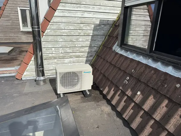 Buitenunit op een plat dak naast een dakraam