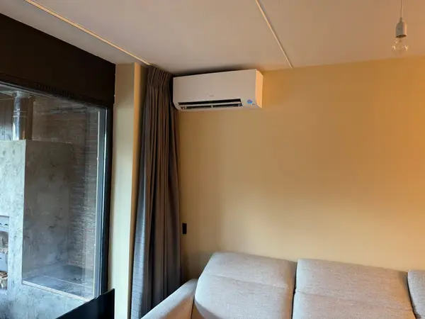Wit airco-binnendeel in een woonkamer met okerkleurige wand