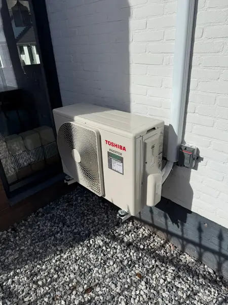 Buitenunit op grind tegen een witte gevel