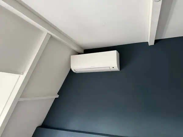Wit airco-binnendeel op een donkergroene wand onder een schuin dak
