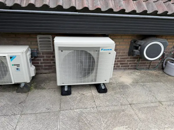 Buitenunit op trillingsdempers naast een garagedeur