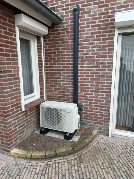 Buitenunit tegen een bakstenen gevel naast een raam