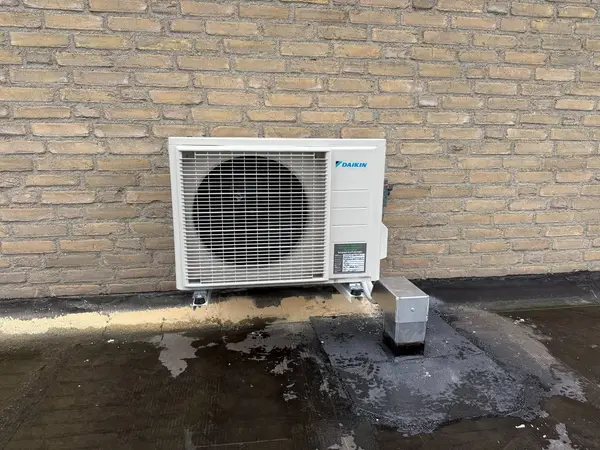 Buitenunit op een plat dak tegen een lichte gevel