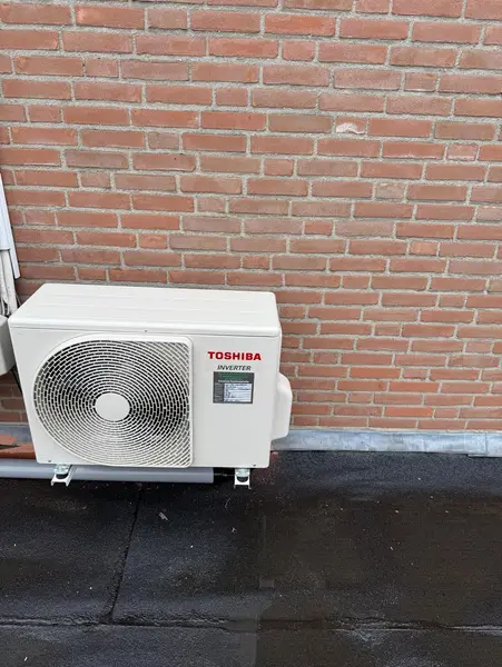 Buitenunit op wandbeugels tegen een bakstenen gevel