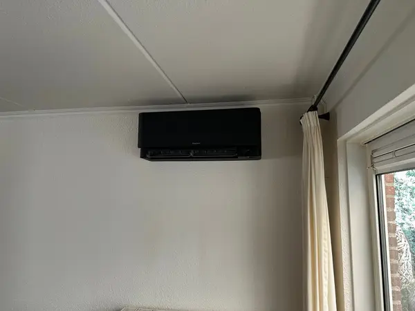 Zwart airco-binnendeel naast een gordijn