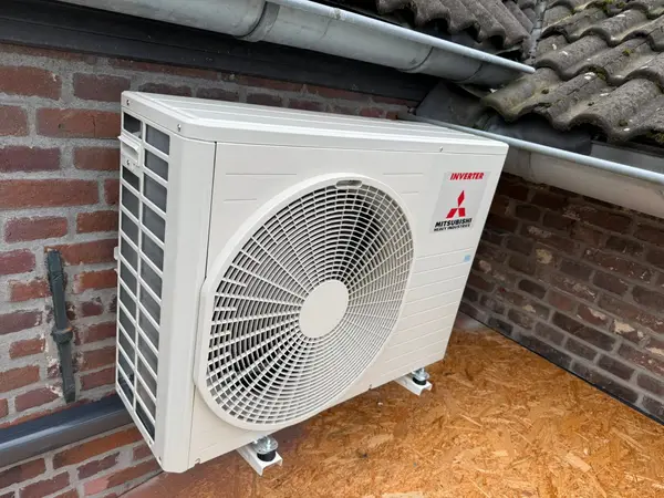 Buitenunit op houtsnippers tegen een bakstenen gevel