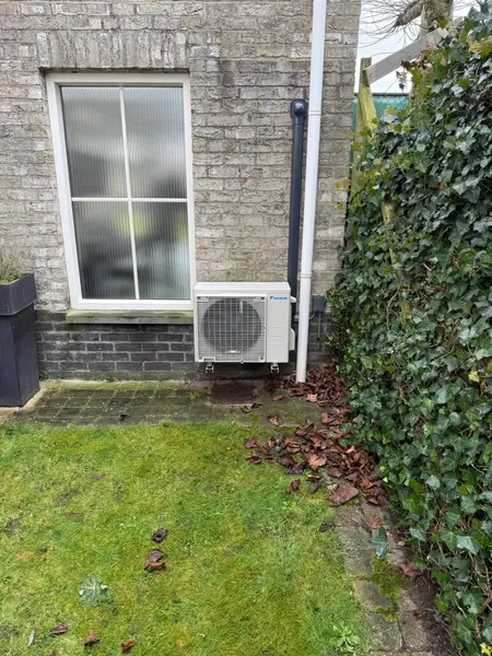 Buitenunit in de tuin naast een bakstenen woning