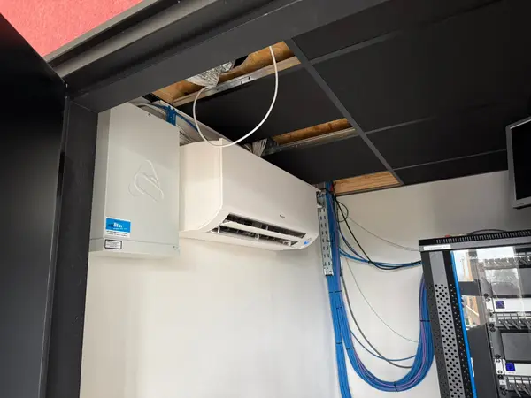 Wit airco-binnendeel onder een donker plafond met nette bekabeling