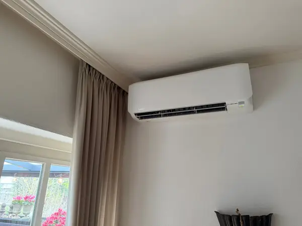 Wit airco-binnendeel naast beige gordijnen