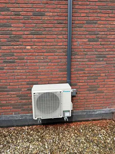 Buitenunit tegen een donkere bakstenen gevel